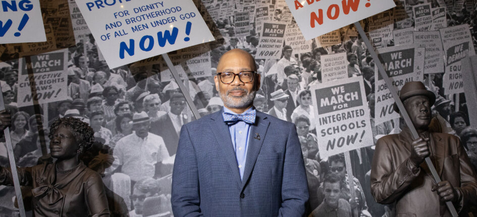 Russell Wigginton in front of all that is a large picture from a crowd of civil rights protesters.