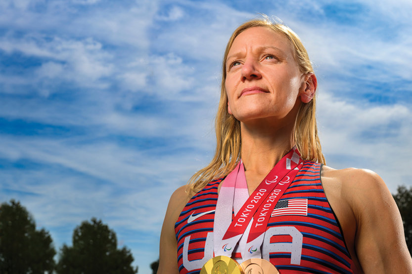 Susannah Scaroni poses on an outdoor track with her Tokyo Paralympics gold and bronze medals around her neck.