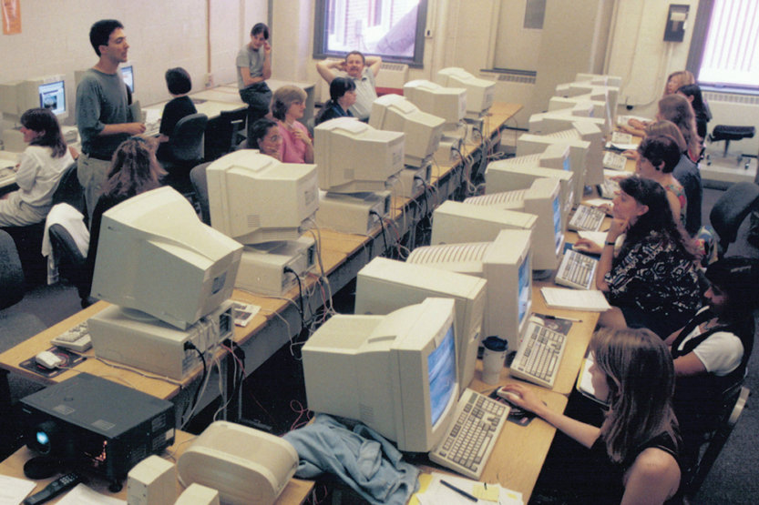 Library science graduate students seated at two rows of tables with beige computers use the internet in class in 1998.