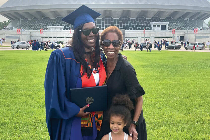 Alexis, in a cap and gown, Gladys and Brooklyn pose in front of State Farm Center.