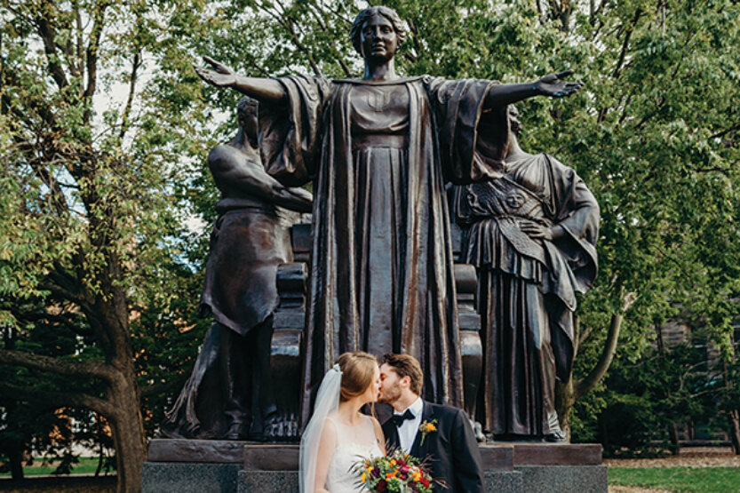 Javan and Melissa Raney Samp kiss in front of the Alma Mater sculpture on their wedding day.