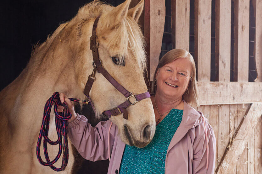 Suzanne Miller poses with a tan horse in a stable