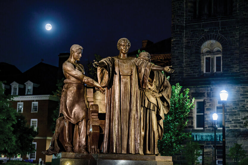 Alma Mater statue at night with moon.