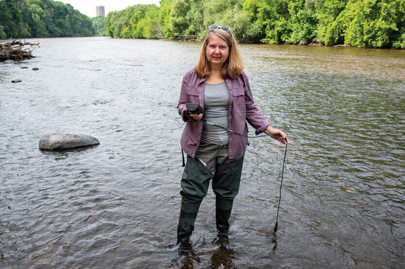 Cheryl Nenn standing in a river holding water monitoring equipment.