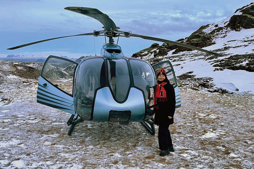 Helen Laka Boen stantds on a snowy mountainside next to a helicopter