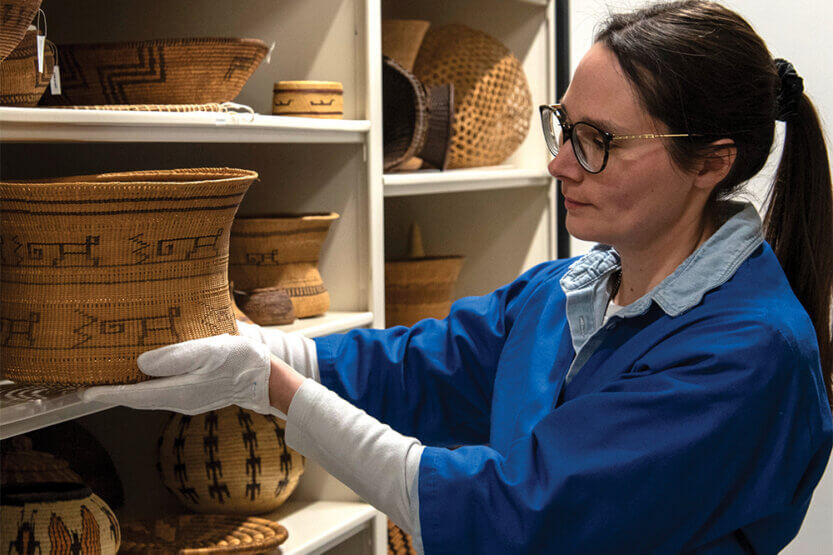 Jennifer Grove holding clay pot among shelves of pottery