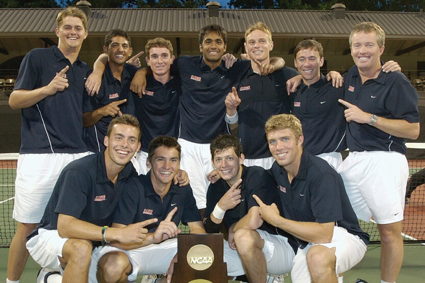 Tennis Champions posed in a group shot on the court with a trophy.